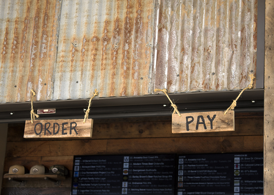 Design details at the bar - custom “order” and “pay’ signs made from wood and rope hang from tin oxidized siding